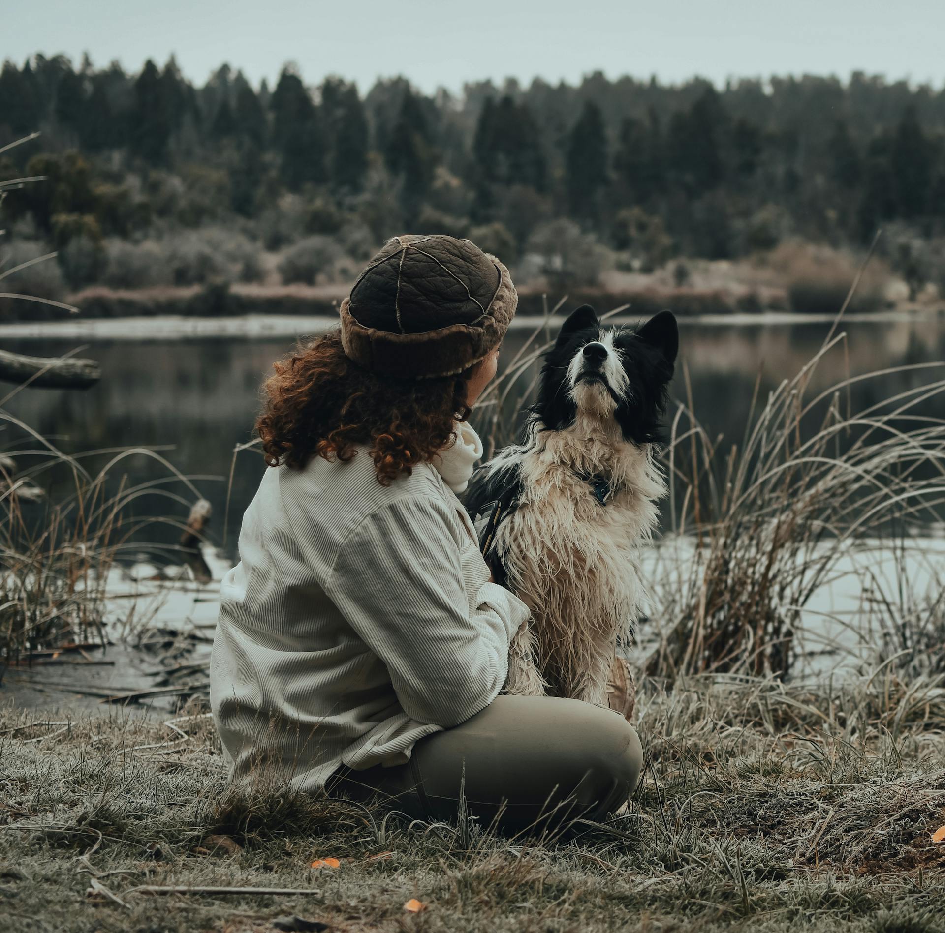 Woman in a Leather Hat Sitting with a Hairy Dog on a Grass