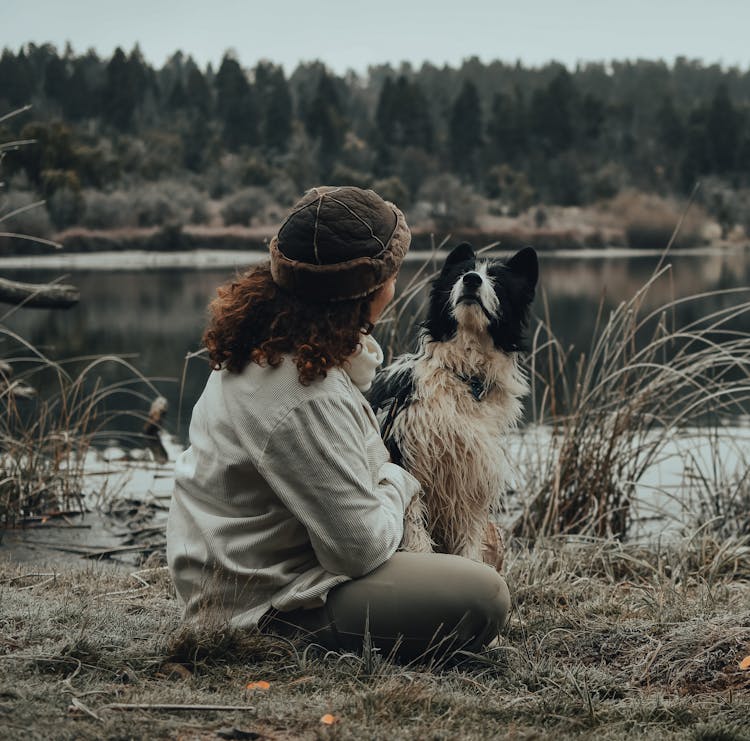 Woman In A Leather Hat Sitting With A Hairy Dog On A Grass