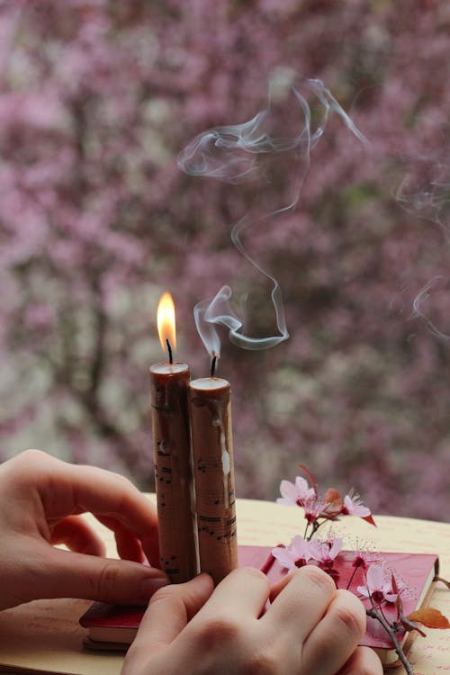 A Person Holding a Lighted Candles Near the Notebook with Flowers