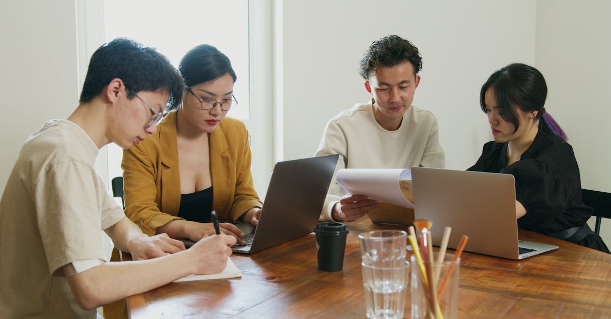 A team of diverse professionals collaborating on laptops and documents in a bright office setting.