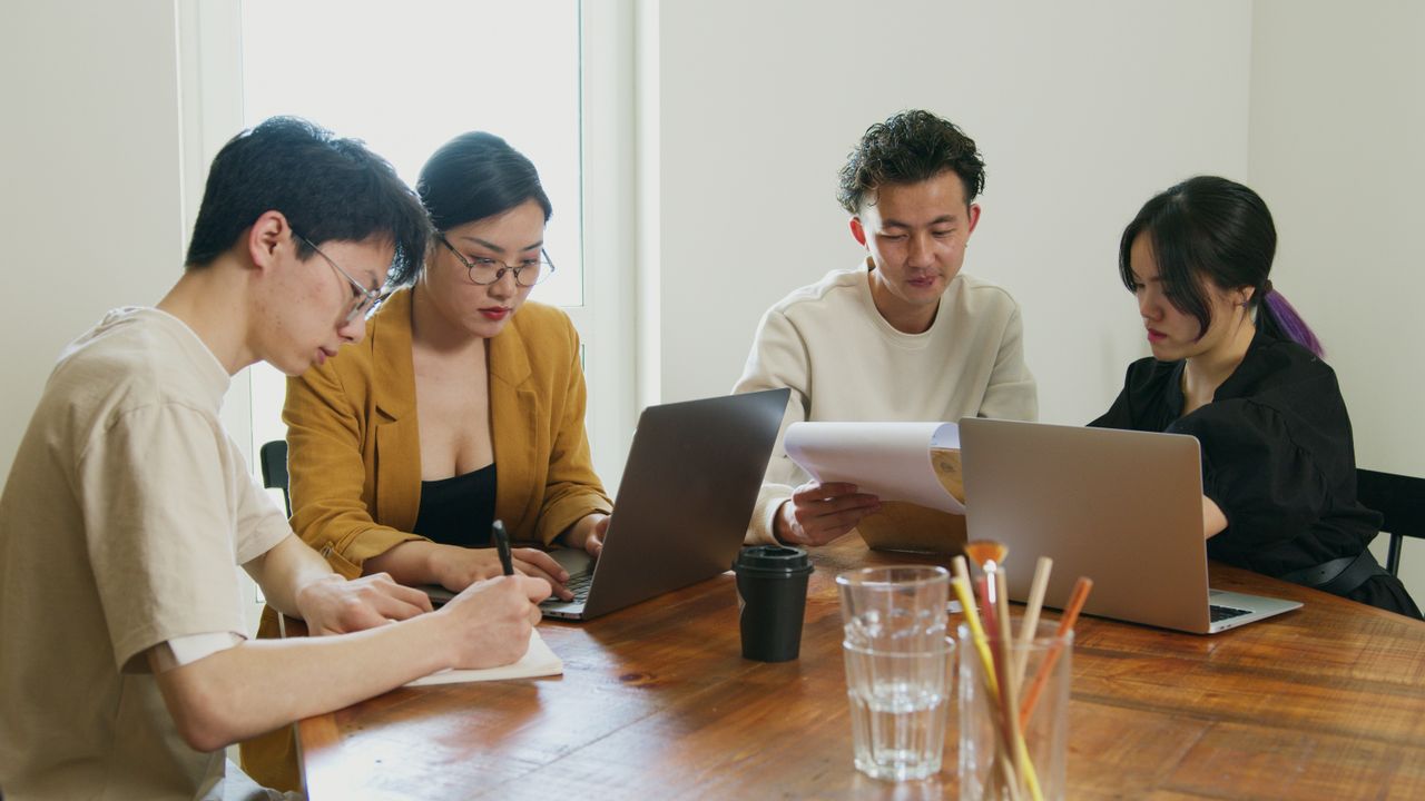 A team of diverse professionals collaborating on laptops and documents in a bright office setting.