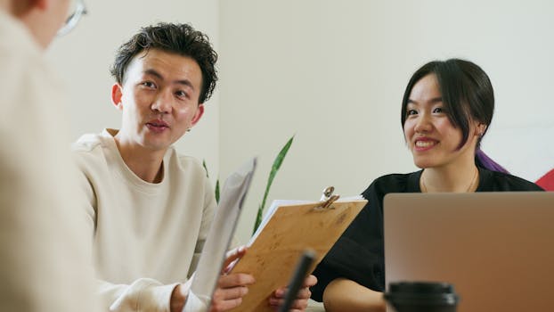 Two colleagues brainstorming at a workplace with laptops, papers, and smiles.
