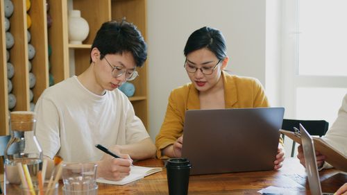 Free Two professionals working together on a laptop and notebook in a bright office space. Stock Photo