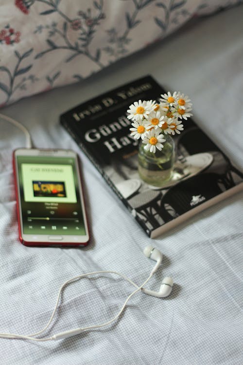 A Mobile Phone with Earphones Near the Flower Vase with Daisies