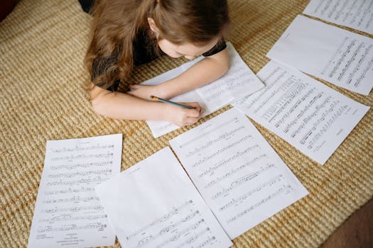 A young girl lying on a carpet writing music notes surrounded by sheets, enjoying a creative moment at home.