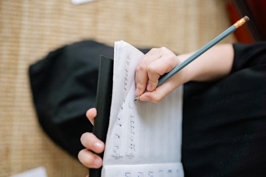 Detailed view of a hand composing music with pencil on sheet paper, creating a musical score.