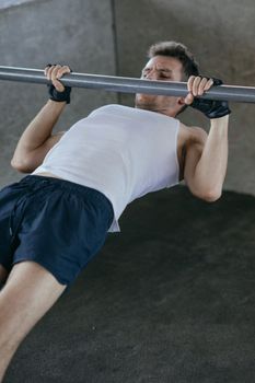 A man wearing fingerless gloves and a tank top performing an inverted row in a gym.