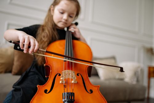 Free Young girl enjoying classical music by playing the cello indoors. Stock Photo