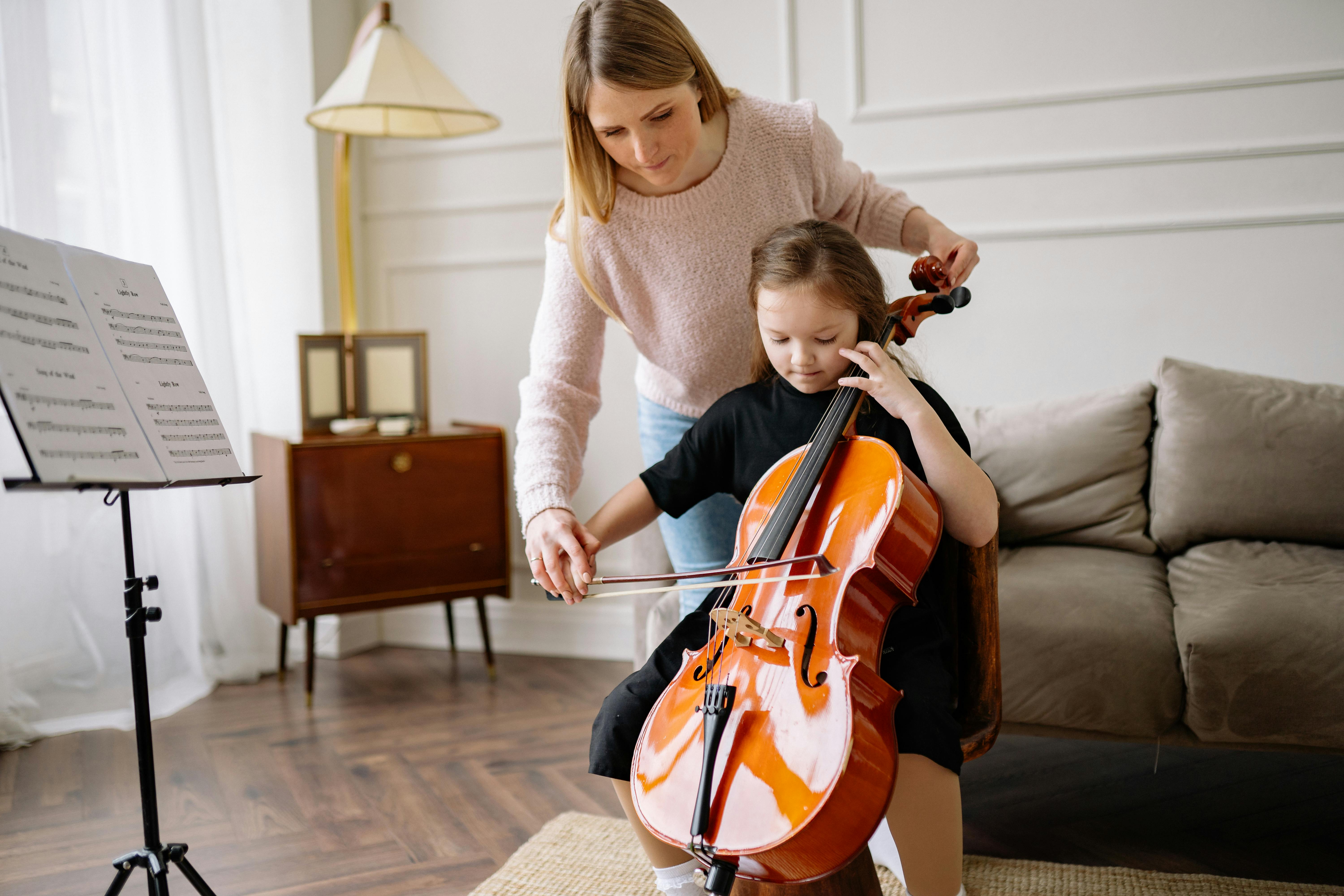 woman in pink sweater teaching a girl to play cello