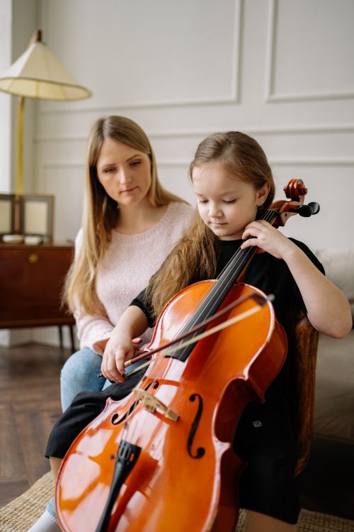 Free Young girl practices cello with attentive teacher in a warm, inviting room. Stock Photo