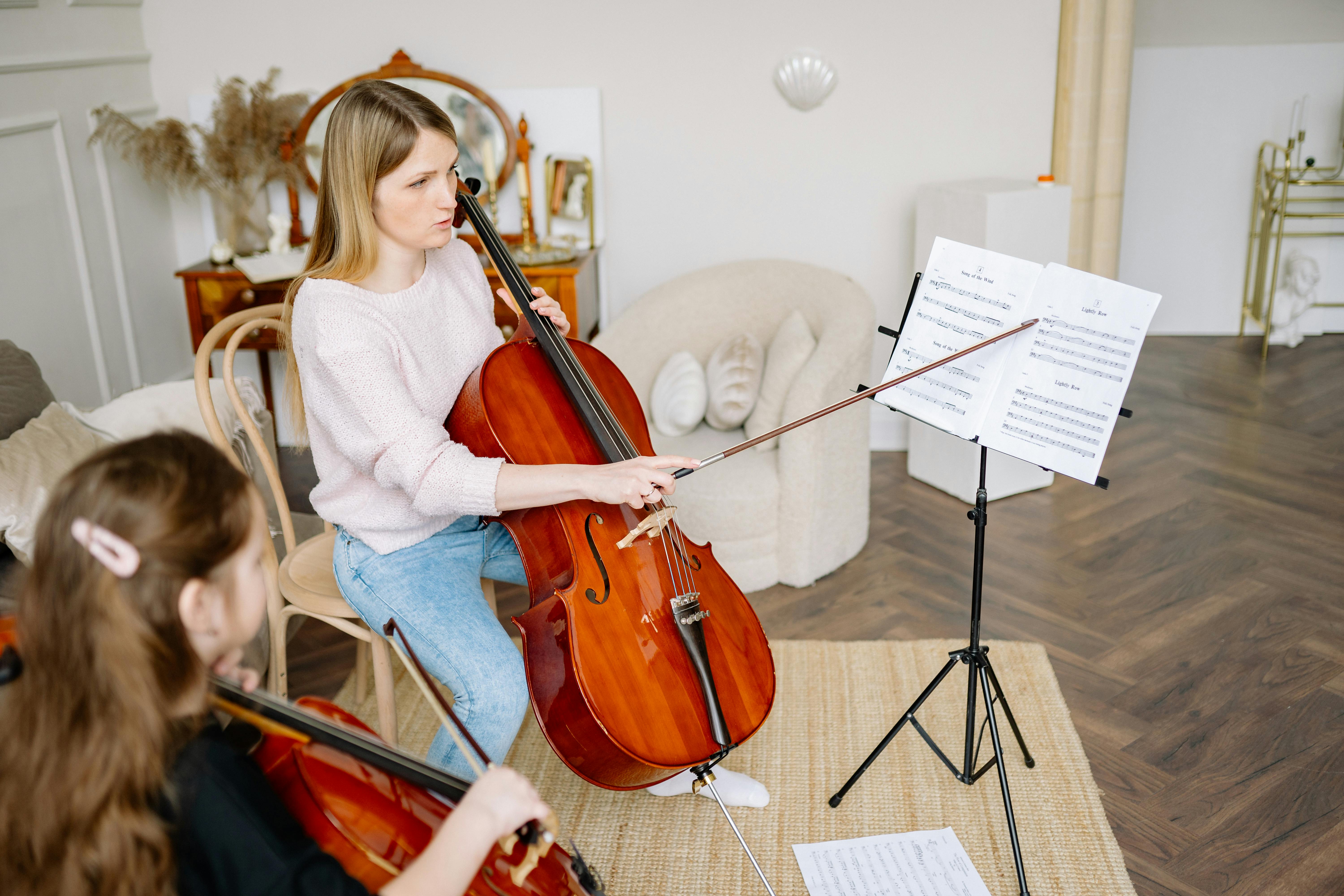 A woman teaching a young girl to play the cello in a cozy home setting.