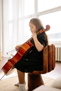 A young girl playing cello in a bright, cozy room, focusing on her music practice.