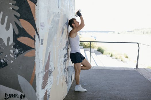 A man wearing sportswear rests against a graffiti wall outdoors, illustrating active lifestyle concepts.