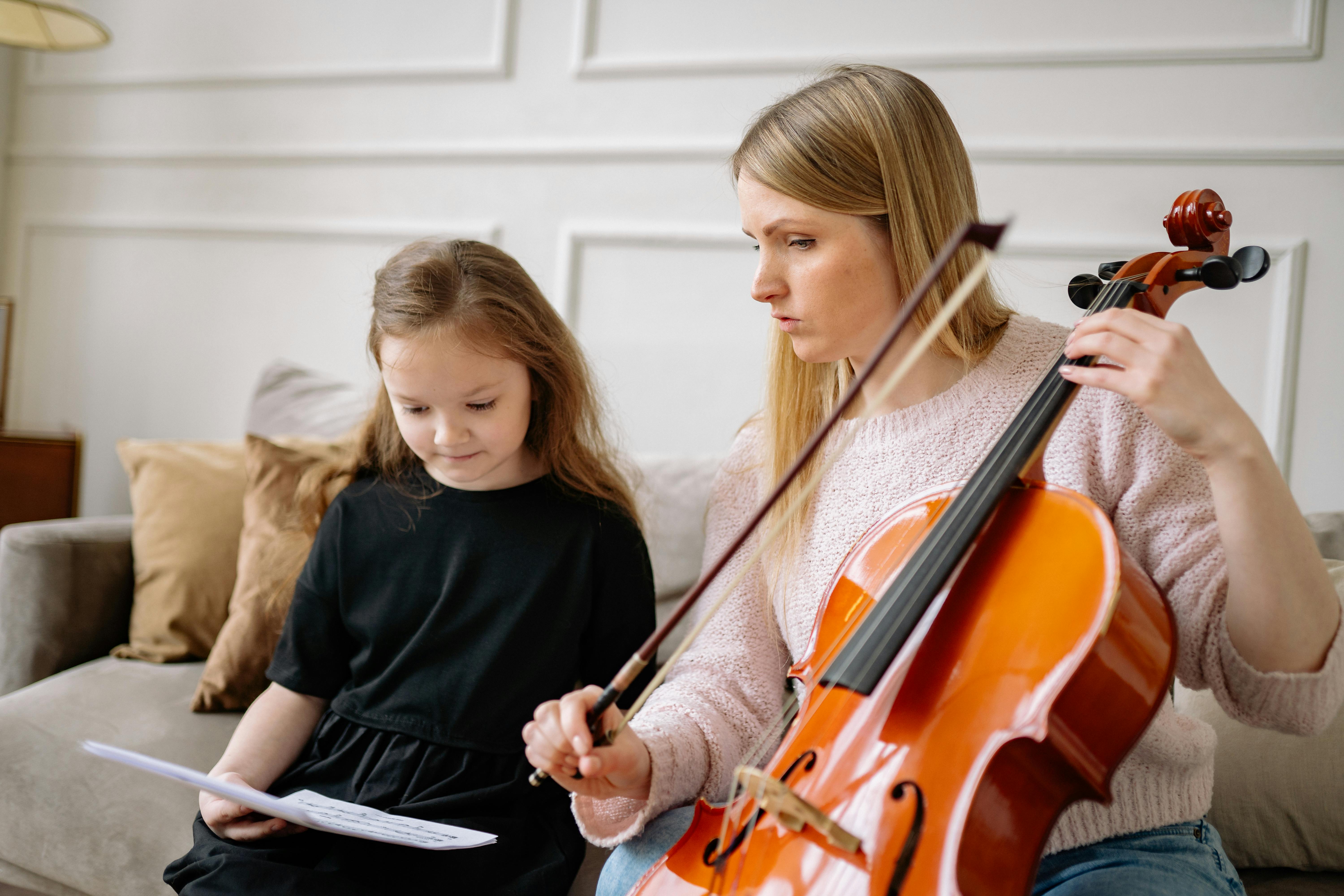 a woman in knitted sweater talking to the girl while holding a cello