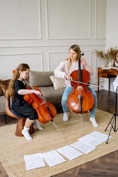 A girl receives a cello lesson from a woman in a cozy living room setting, focused on music learning.