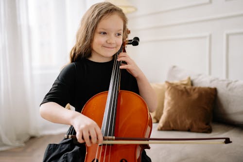 Free A Young Girl in Black Dress Smiling while Playing Cello Stock Photo