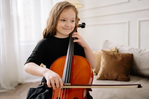 Free A cute girl in a black dress plays the cello indoors, smiling happily. Stock Photo