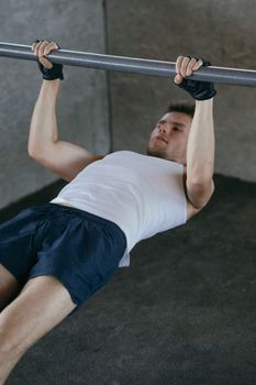 Adult man working out indoors wearing a white tank top and fingerless gloves