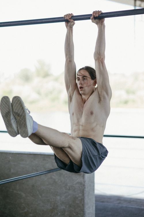Free Shirtless man exercising with a hanging leg raise, promoting strength and fitness outdoors. Stock Photo