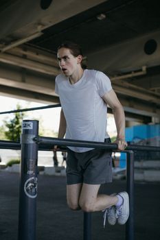 Young man performing dips on parallel bars under a bridge, showcasing strength and endurance.