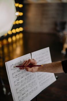 A person pointing at sheet music with a pencil in a cozy music class setting.