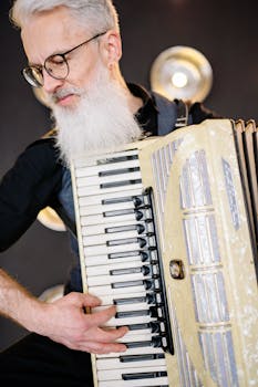 Senior musician with a white beard playing an accordion indoors.
