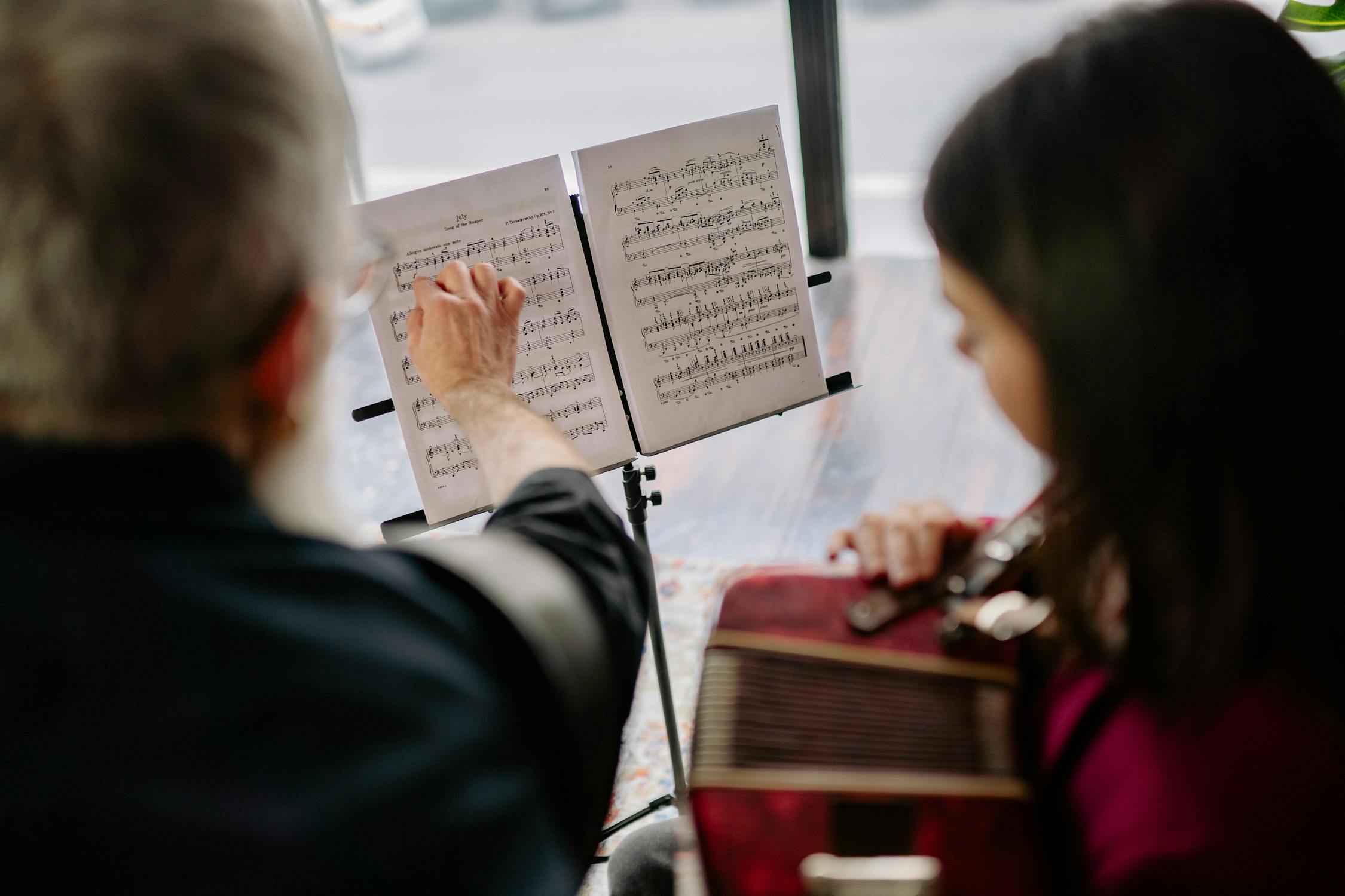 Man Pointing at Notes on a Music Sheet and Girl Playing an Instrument ...