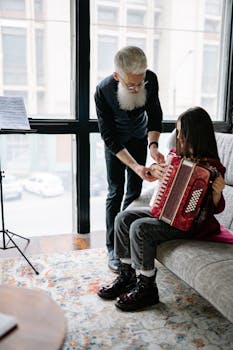 An older man teaches a young girl how to play the accordion indoors.