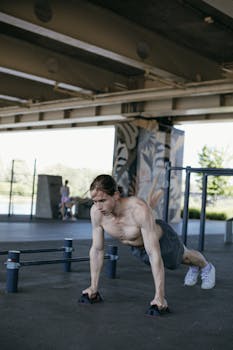 Athletic man doing push-ups outdoors in an urban gym setting, showcasing physical strength and fitness.