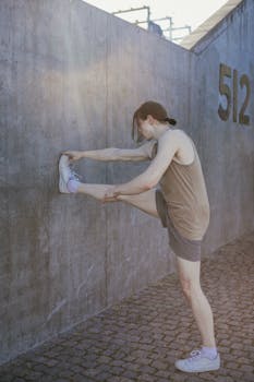 A young adult performs a wall stretch outdoors as part of a fitness routine.