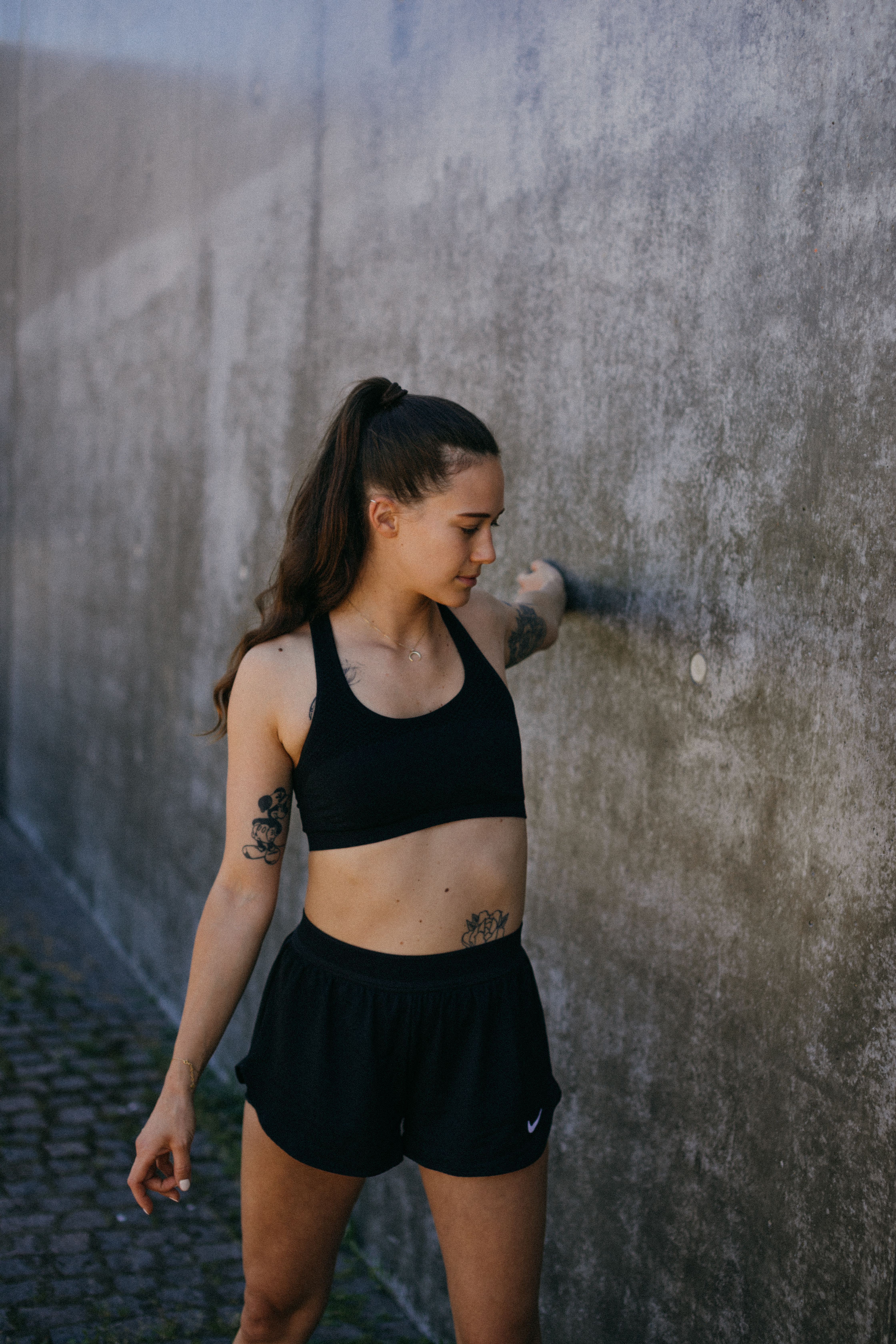 A young woman in sportswear stretching against a concrete wall, embodying a healthy lifestyle.