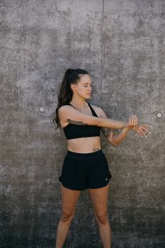 Woman in activewear stretching outdoors in front of a concrete wall.