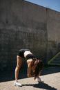 Woman in Black Sports Bra and Black Shorts Bending Her Body on Gray Concrete Wall during