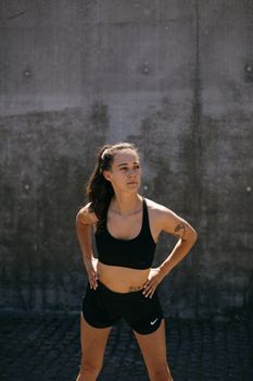 A determined woman in activewear posing confidently outdoors against a concrete wall.