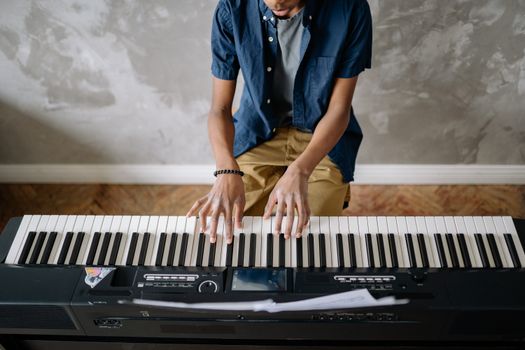 A man in casual attire plays an electric keyboard indoors, focusing on the music.