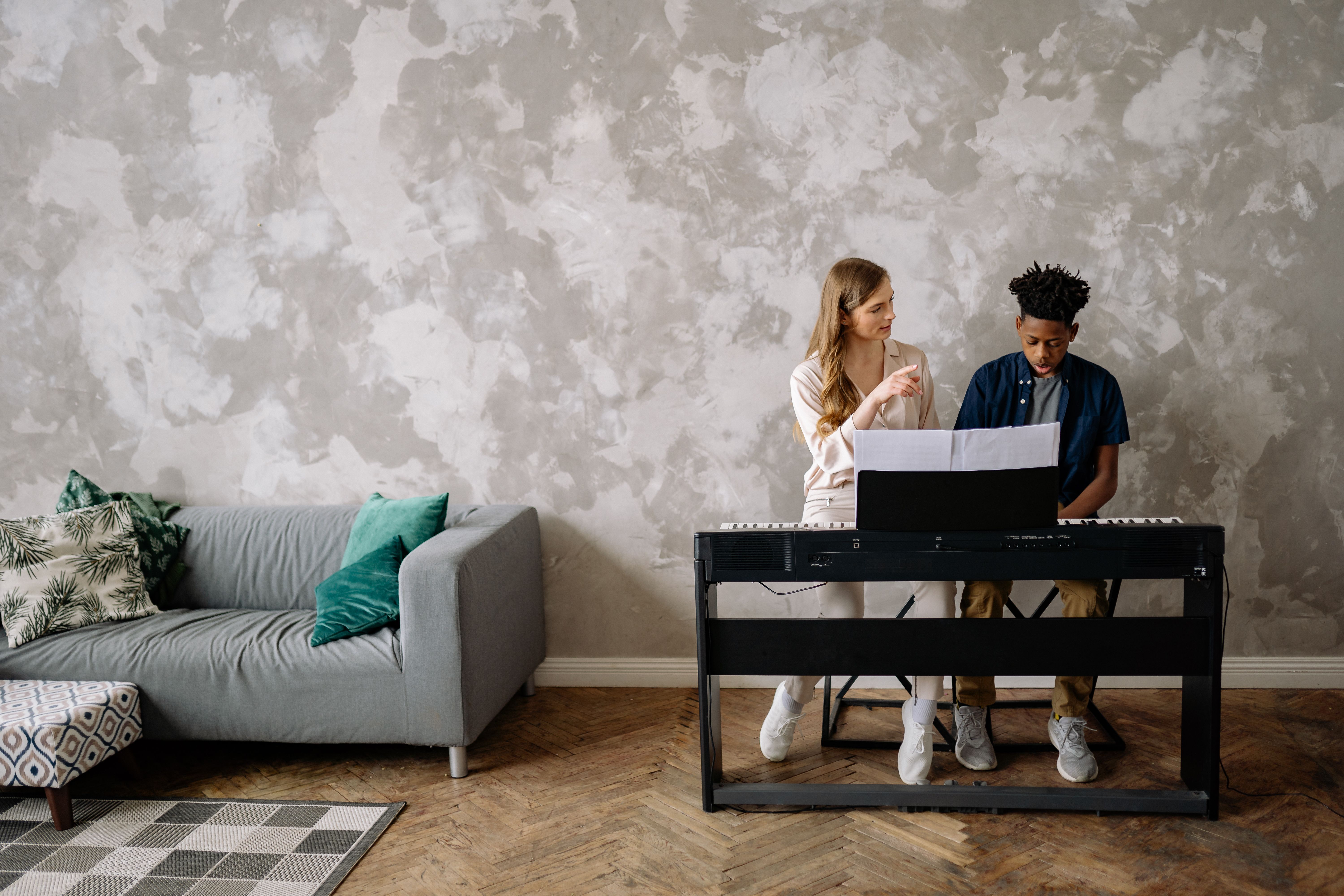 A woman instructing a boy at the piano in a cozy home setting.