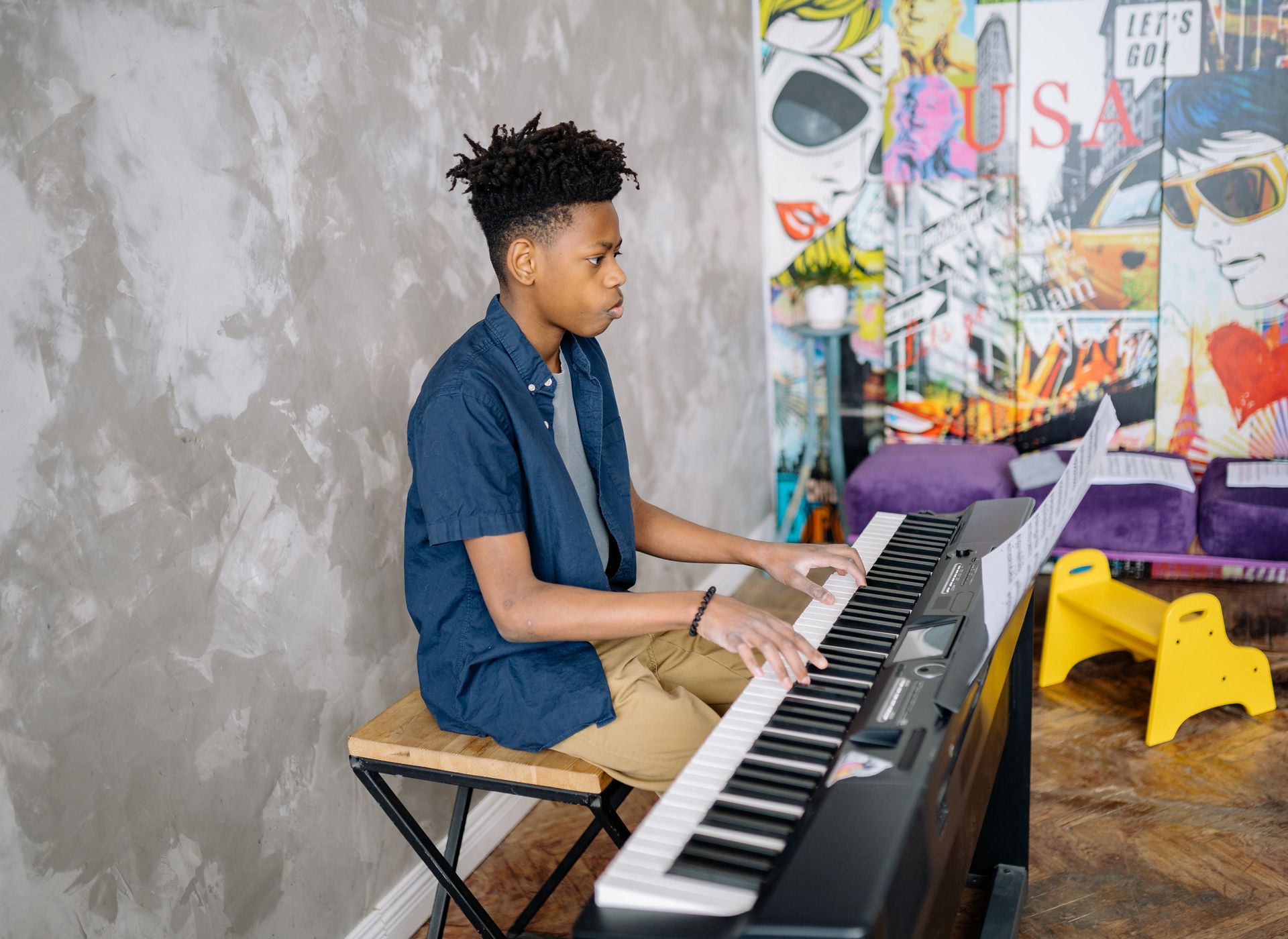 Black teenager practicing piano in a colorful indoor setting with artistic decor.