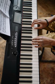 High angle view of hands playing an electronic keyboard with sheet music on top.