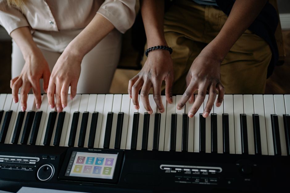 A close-up of two people playing piano together indoors, showcasing their hands and fingers.