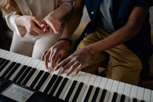 Free Close-up of teacher and student during piano lesson focusing on hand placement. Stock Photo