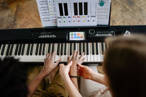 Free A woman guides a student's hands on a keyboard piano, emphasizing musical instruction. Stock Photo