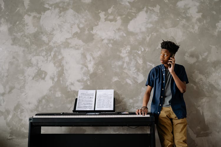 A Young Boy Leaning On The Wall While Talking On The Phone Near The Piano