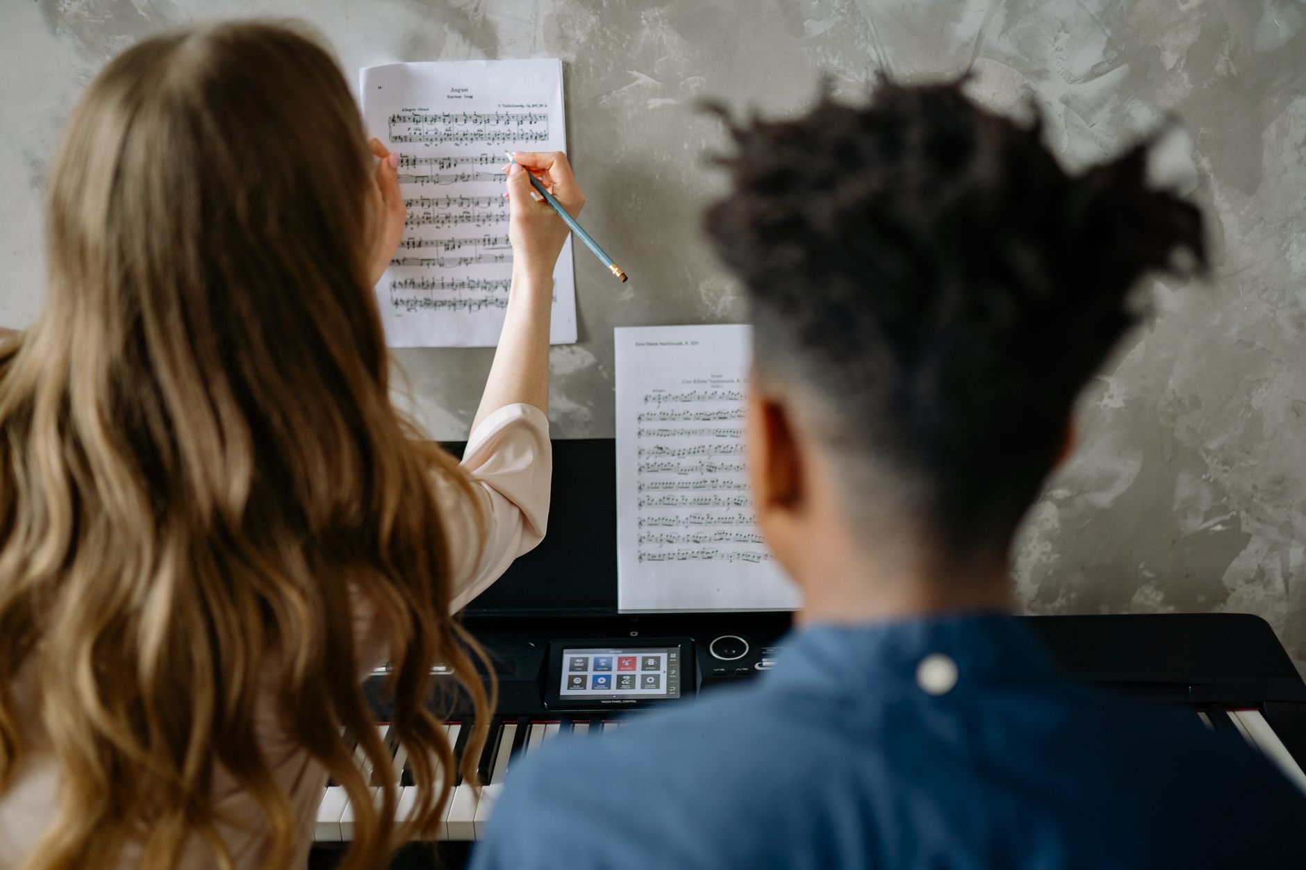A student and teacher in a music lesson focusing on piano sheet music indoors.