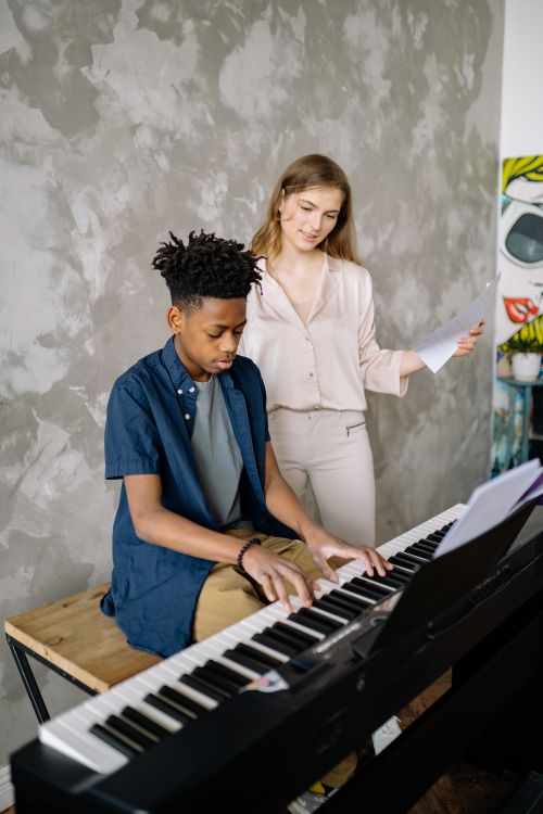 Free A young boy receives piano lessons from a teacher in a cozy home setting, focusing on music learning. Stock Photo
