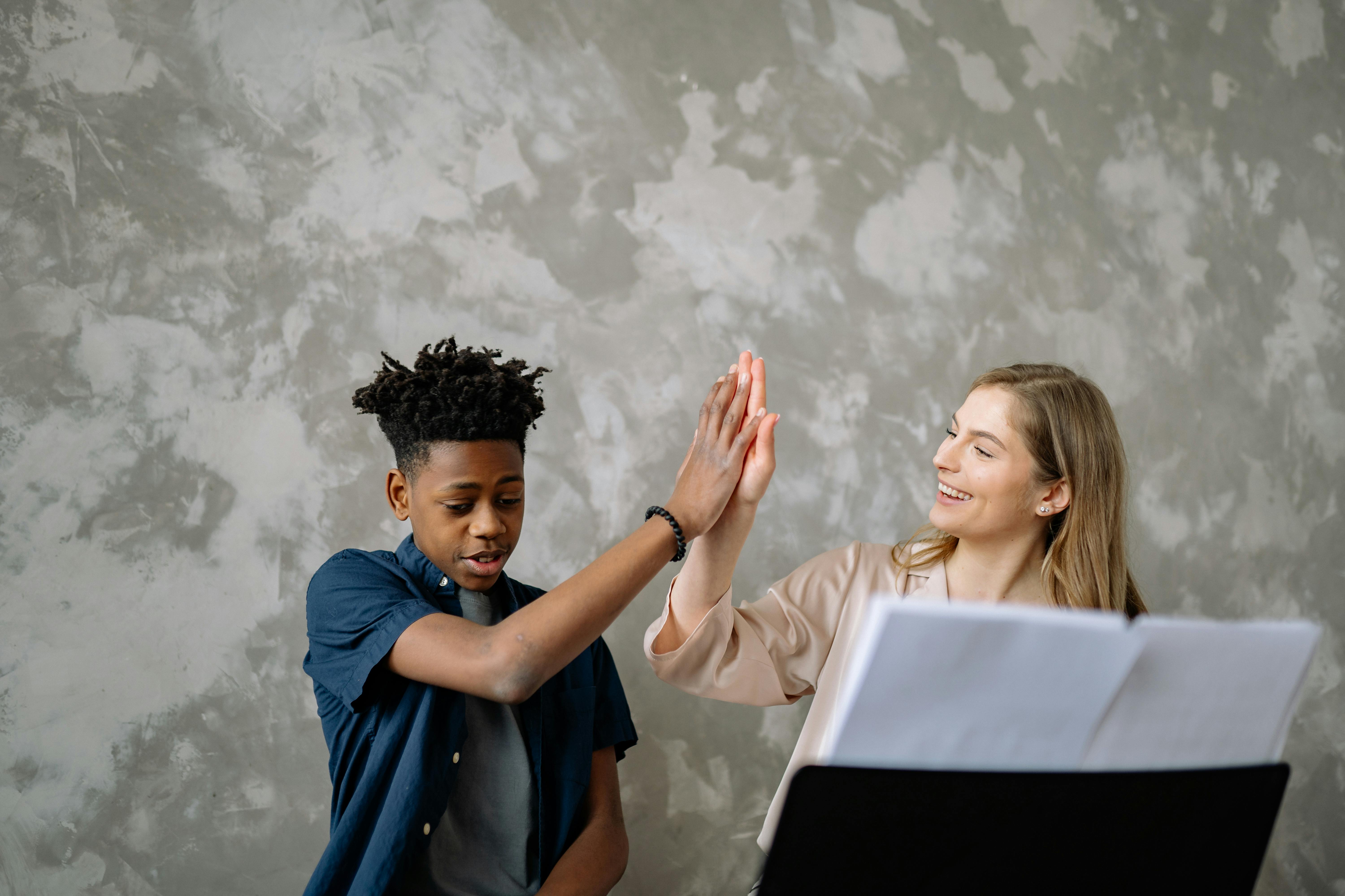A child and teacher celebrate success with a high five during piano lessons, ensuring a positive learning environment.