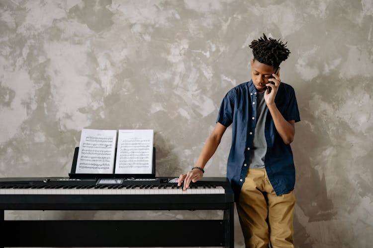 Boy Talking On The Phone While Pressing An Electric Keyboard Key