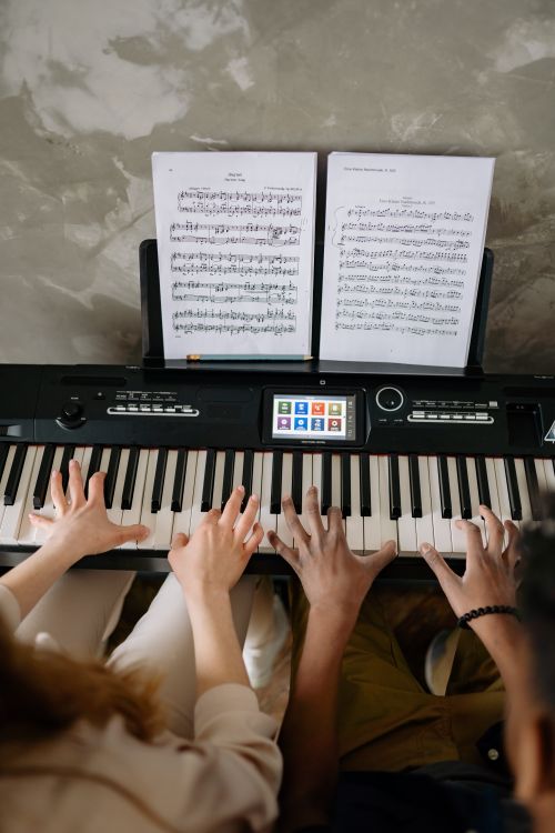Free Top view of two people playing duets on a digital piano during music lessons. Stock Photo