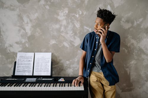Free A Boy in Blue Shirt Standing Near the Piano while Talking on the Phone Stock Photo