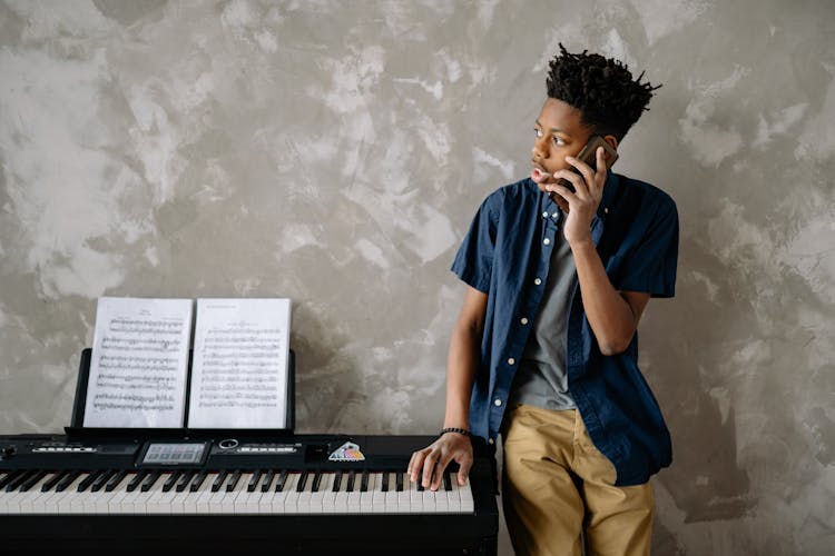 A Boy In Blue Shirt Standing Near The Piano While Talking On The Phone