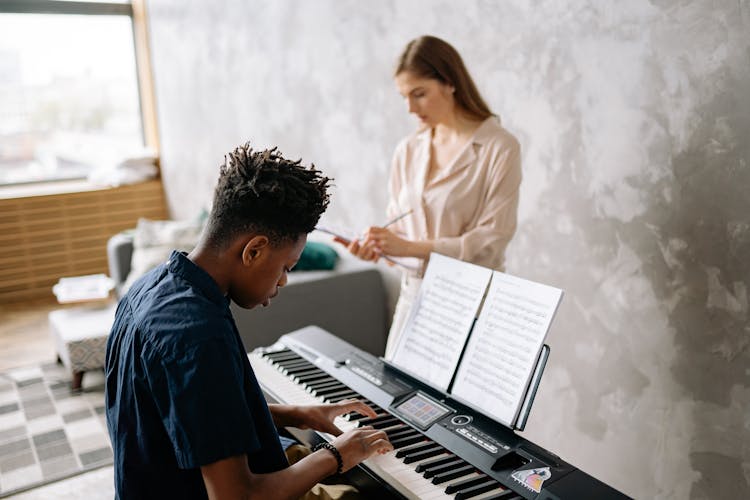 Boy Playing The Piano While Teacher Writing On A Note